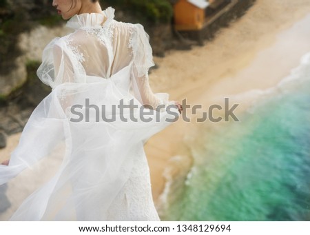 beautiful bride with a long developing veil stands on the beach by the ocean
