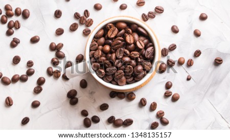 White cup full of coffee beans with wooden stand on a light gray table background.