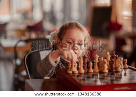 Portrait Caucasian Little cirly girl playing chess at the table in interior with chessboard  at competition early childhood development