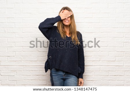 Blonde woman over brick wall covering eyes by hands. Surprised to see what is ahead