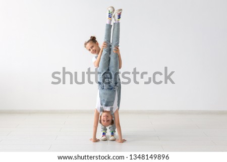 Family and sport concept - Two acrobat twin girls are standing on the hands over white background