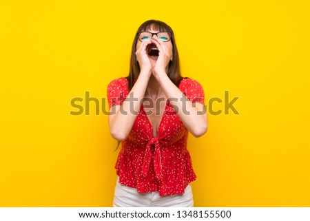 Young woman over yellow wall shouting and announcing something
