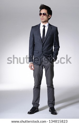 Full body young businessman in sunglasses standing on light background