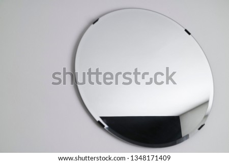 Interior close up of circular mirror with black metal clips. Wall mounted mirror surface with geometric black and white pattern in reflection. Off centre composition for effect.