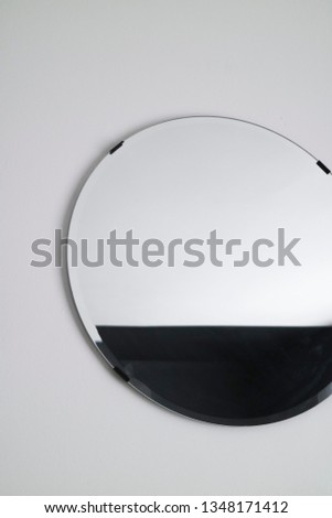 Interior close up of circular mirror with black metal clips. Wall mounted mirror surface with geometric black and white pattern in reflection. Off centre composition for effect.