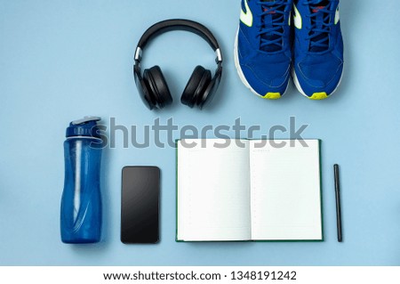 Men's blue sneakers, bottle of waters, smartphone, headphone, notebook diary with marker on blue background Top view flat lay copy space. Concept of an active lifestyle, sports, fitness, health