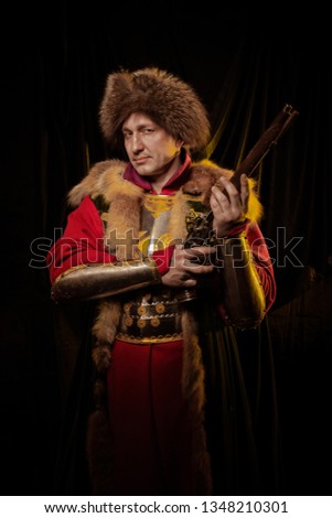 Medieval man in knight's armor and ancient red dress with furs in the yellow light on a dark background