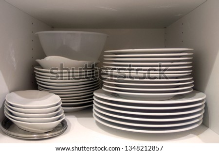 Dishes in cupboard in the kitchen. White plates and bowls stacked in a cupboard in the kitchen.