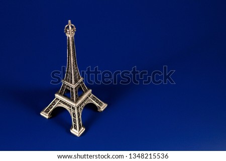 Eiffel tower statuette on blue background. Famous historical landmark in Paris. Architecture souvenir from capital city of France. Concept for tourism/travelling and sightseeing.