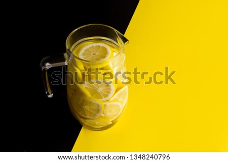 A transparent glass jar filled with lemon slices on a yellow and black beckground. Colors contrast and harmonize at the same time.