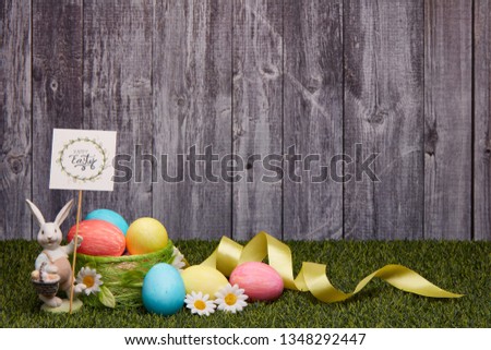 Colored easter eggs, easter rabbit and flowers lying on a green grass on a grey wooden  background with copy space. Greeting card, Easter background