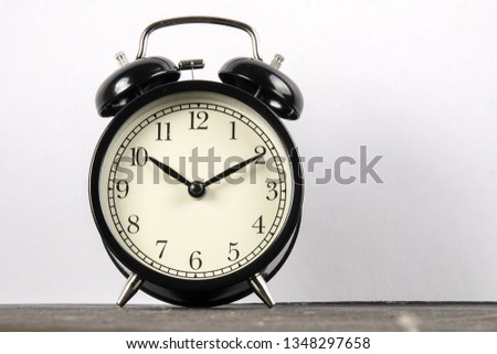 Black alarm clock on the wooden surface against the white background.