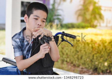 Asian special child on wheelchair is having sad thoughts with natural light, outdoor background.