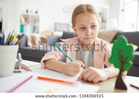 Portrait of cute girl doing homework at home and looking away thinking, copy space