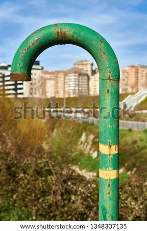 curved green metal pipe with traces of rust for the air outlet of the urban gas pipeline, with some city buildings in defocused background