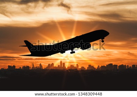 silhouette of commercial plane flying over a city during with lights sunset