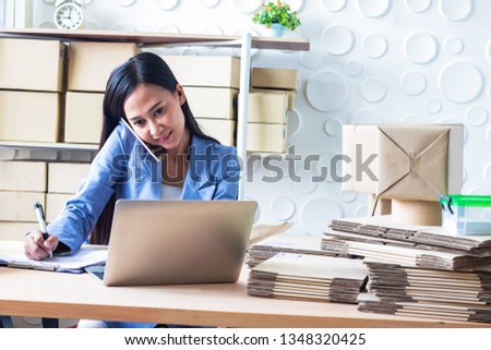 The young  Asia Businesswoman.She is writing and use mobile phone. She makes it for order online. She is happy and smiles. Gift , Business, Photo concept work and Shopping.