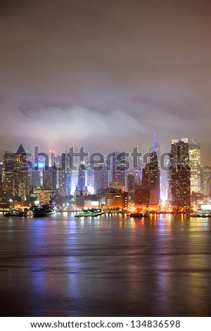 New York City Manhattan midtown Times Square skyline at night with skyscrapers over Hudson River viewed from New Jersey.