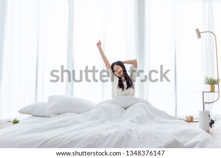 Asian woman wake up in the morning, sitting on white bed and stretching, feeling happy and fresh Royalty-Free Stock Photo #1348376147