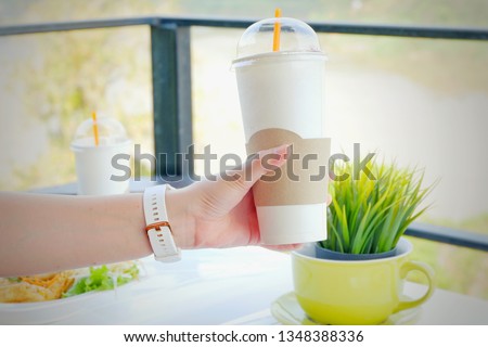 Hand holding ice coffee in restaurant on mountain and river background. 