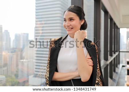 Successful asian business woman standing against a window in modern office with city view.. 