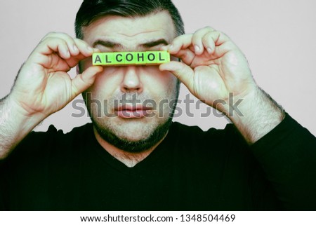 Words - ALCOHOL with YELLOW blocks. young man holds  cubes befor her eyes. isolated on white background. 