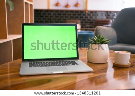 Laptop with green screen on a chic coffee table with a cappuccino and cactus plant on it