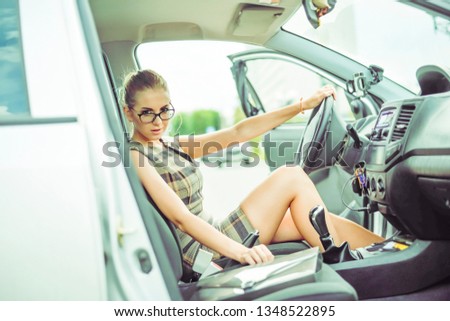 Beautiful girl in stylish glasses sit down inside car. Businesswoman is opening door of vehicle and preparing to sitting in the driver seat. Business woman is looking indoor with plastic suit case