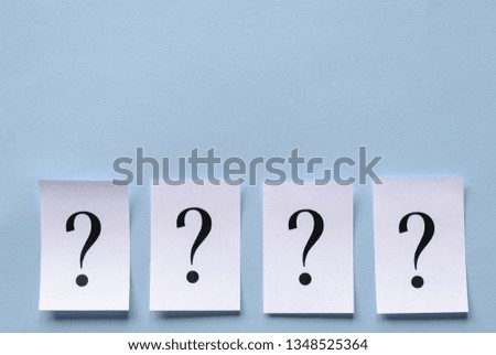 Four printed question marks on white paper forming a lower border on a blue background neatly laid in a row with three dimensional drop shadow and copy space