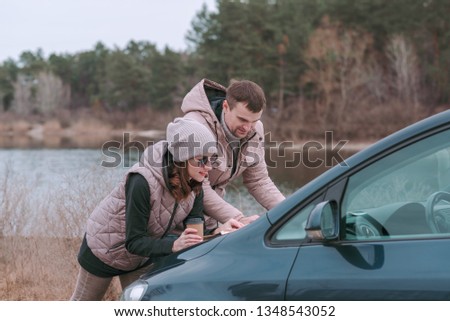 Young romantic couple is watching road map on hood of car near the river.