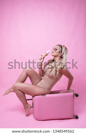 Young pretty girl blond woman posing on pink background with suitcase and ice cream in hands.