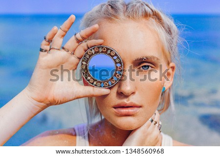 beautiful young fashion model on the beach. Close up portrait of boho model holding small mirror at her eye