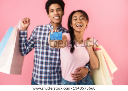 Happy teenage couple showing credit card and holding shopping bags, pink background