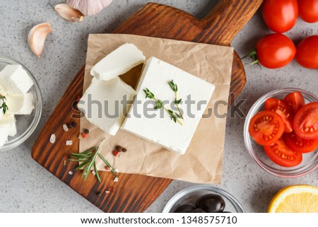 Chopped feta on wooden board, herbs, olives and tomatoes on concrete background. Homemade greek cheese concept