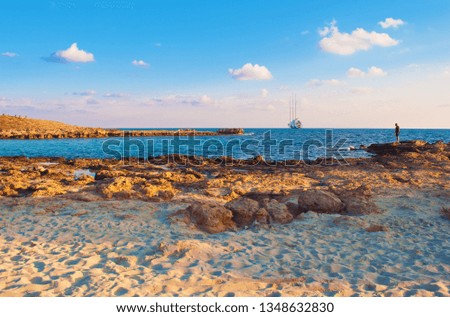 Image of breathtaking Nissi beach in Agia Napa, Cyprus. Yellow sand and reefs against blue calm water on a warm evening in fall, small clouds in the sky. Shot during golden hour
