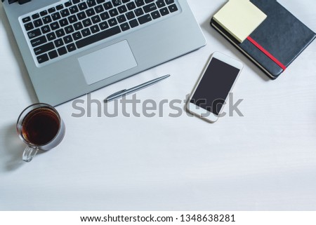 Top view of laptop, black notebook, cellphone, pen, a cup of tea on white wooden table. Workplace of businessman or officer