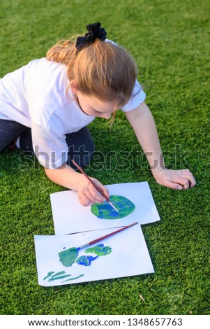 Beautiful little girl drawing with acrylic color a picture of earth globe. Child painting with brush and color a picture of earth. Earth day, plastic free and zero waste concept.