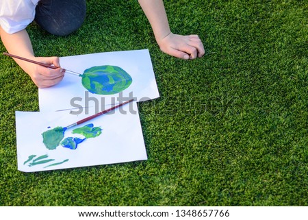Close up kids hand drawing a picture of earth globe.Child painting with brush and watercolor paints a picture of earth.Earth day, plastic free and zero waste concept.