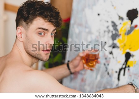 selective focus of handsome artist holding glass of whiskey and looking at camera