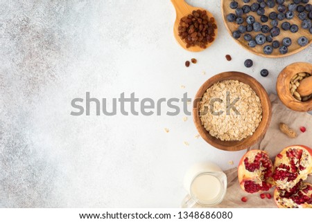Top view and flat lay of oatmeal porridge in wooden ware with milk, red currant, blueberries, almonds, and garnet on textured concrete light table. Mock-up of food for healthy breakfast, flatlay