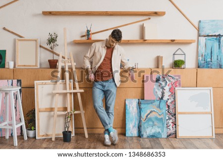 handsome artist in pink shirt and blue jeans standing in spacious gallery
