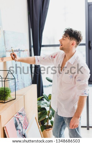 inspired artist in white shirt standing in front of picture in painting studio