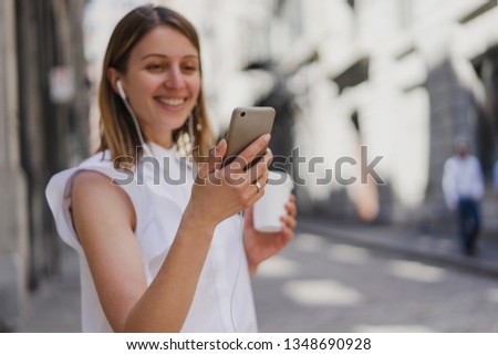 Woman drinking coffee outdoors using modern smartphone device, Happy woman listening to music while going to work