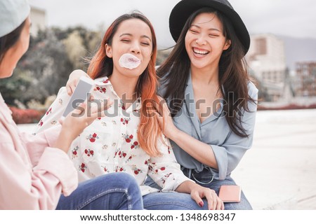 Trendy asian girls making video story for social network app outdoor - Young women friends having fun making live feed - New technology trends and friendship concept - Focus on person blowing Royalty-Free Stock Photo #1348698347