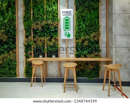 Free Charging Station with green and natural decoration and some wooden stools in public waiting area inside office building. 