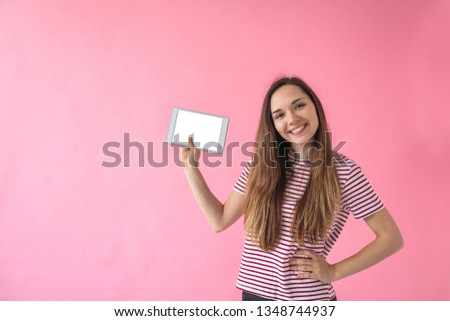 A girl holds in her hand a tablet with a blank screen on a pink background.