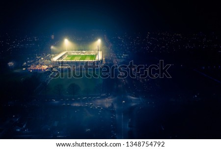 A skyline/horizon view with a football stadium seen from above on a foggy night with the stadium lights on and sporters playing soccer.