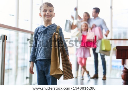 Boy with paper bags shopping at the mall with family in the background