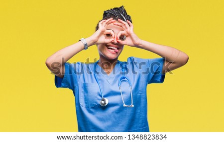 Young braided hair african american girl professional surgeon over isolated background doing ok gesture like binoculars sticking tongue out, eyes looking through fingers. Crazy expression.