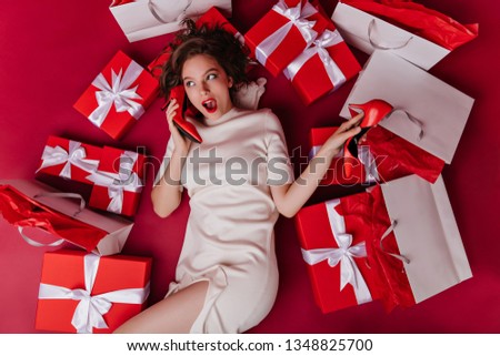 Overhead portrait of graceful lady posing after shopping. Indoor photo of funny female model lying on the floor with gifts.